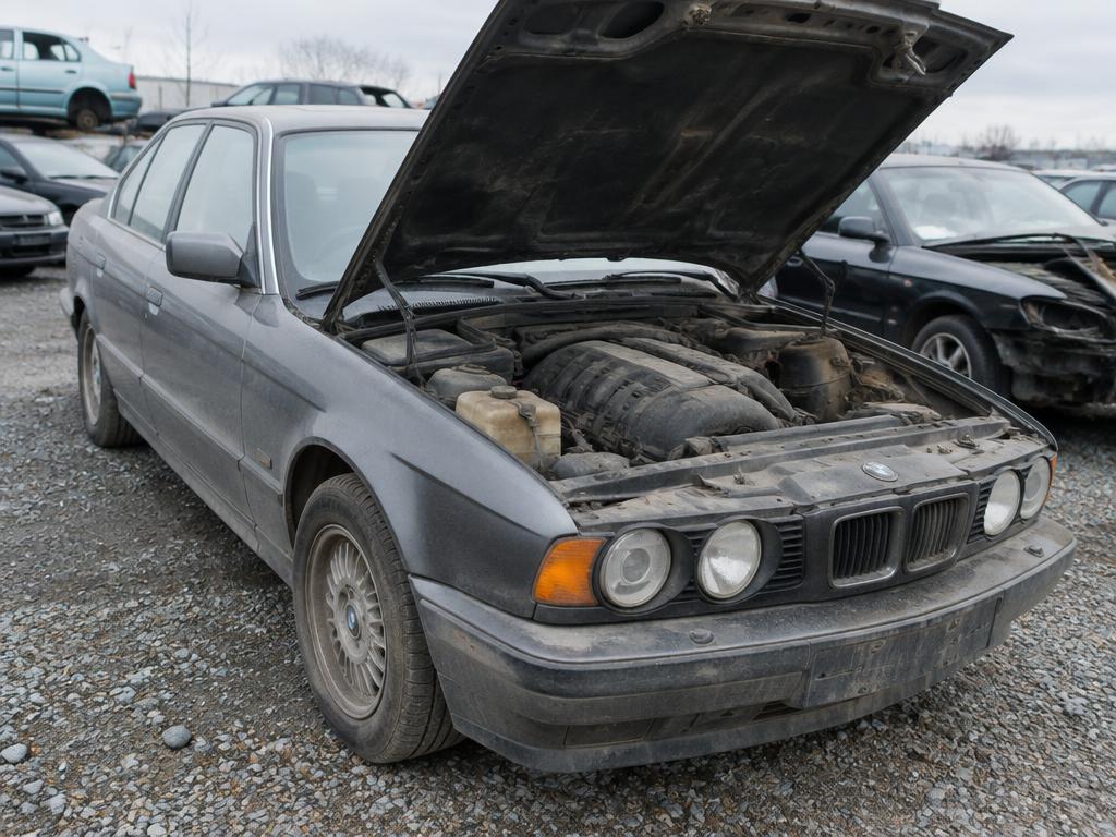 Oude grijze BMW met geopende motorkap en motorschade